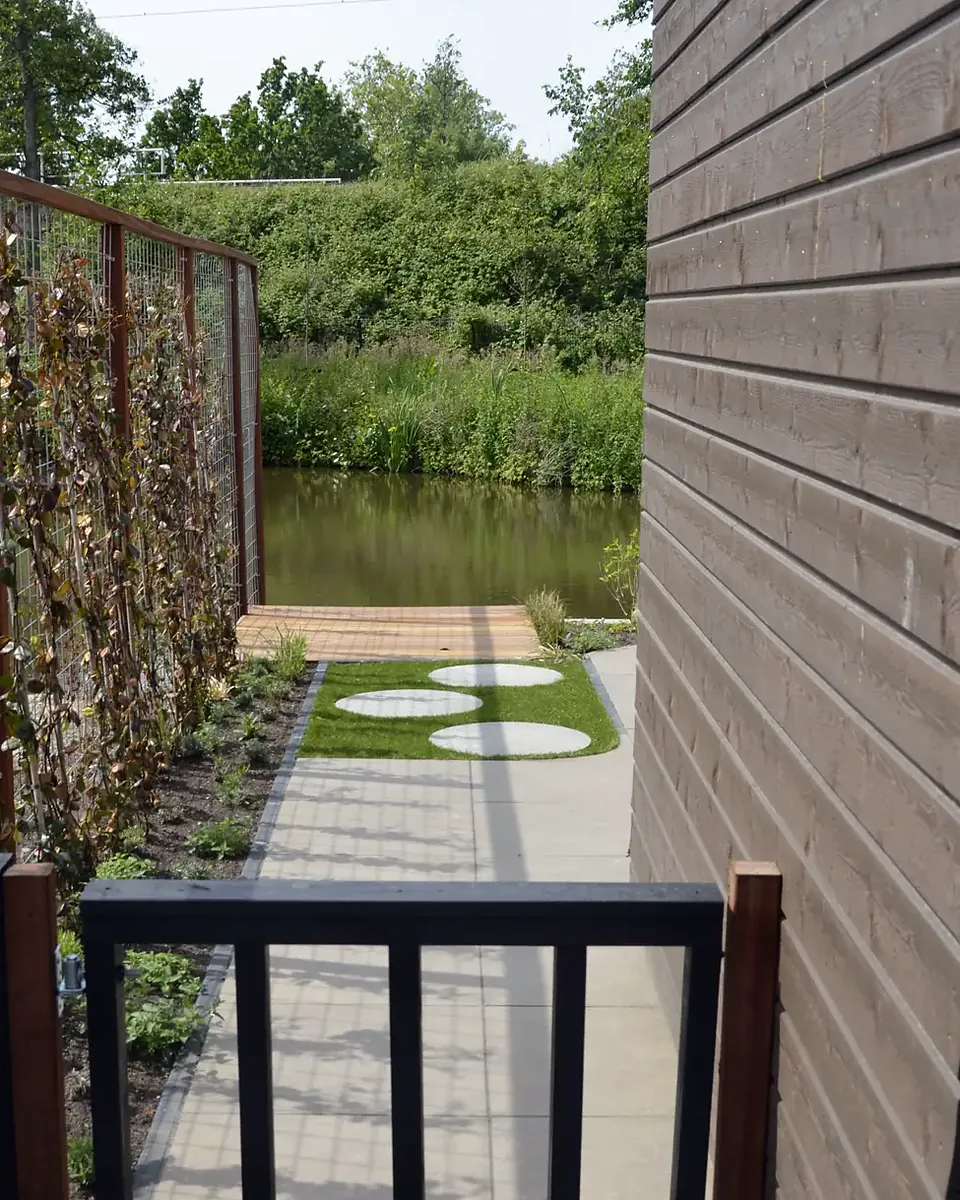 Ná: tegelpad en gazon met ronde stapstenen langs de gevel naar het water