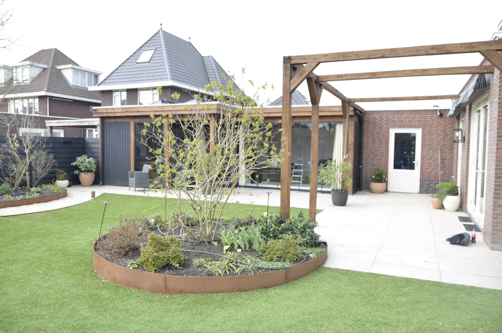 De overkapping staat er, de tuin eromheen is nog zand met gereedschap en een kruiwagen