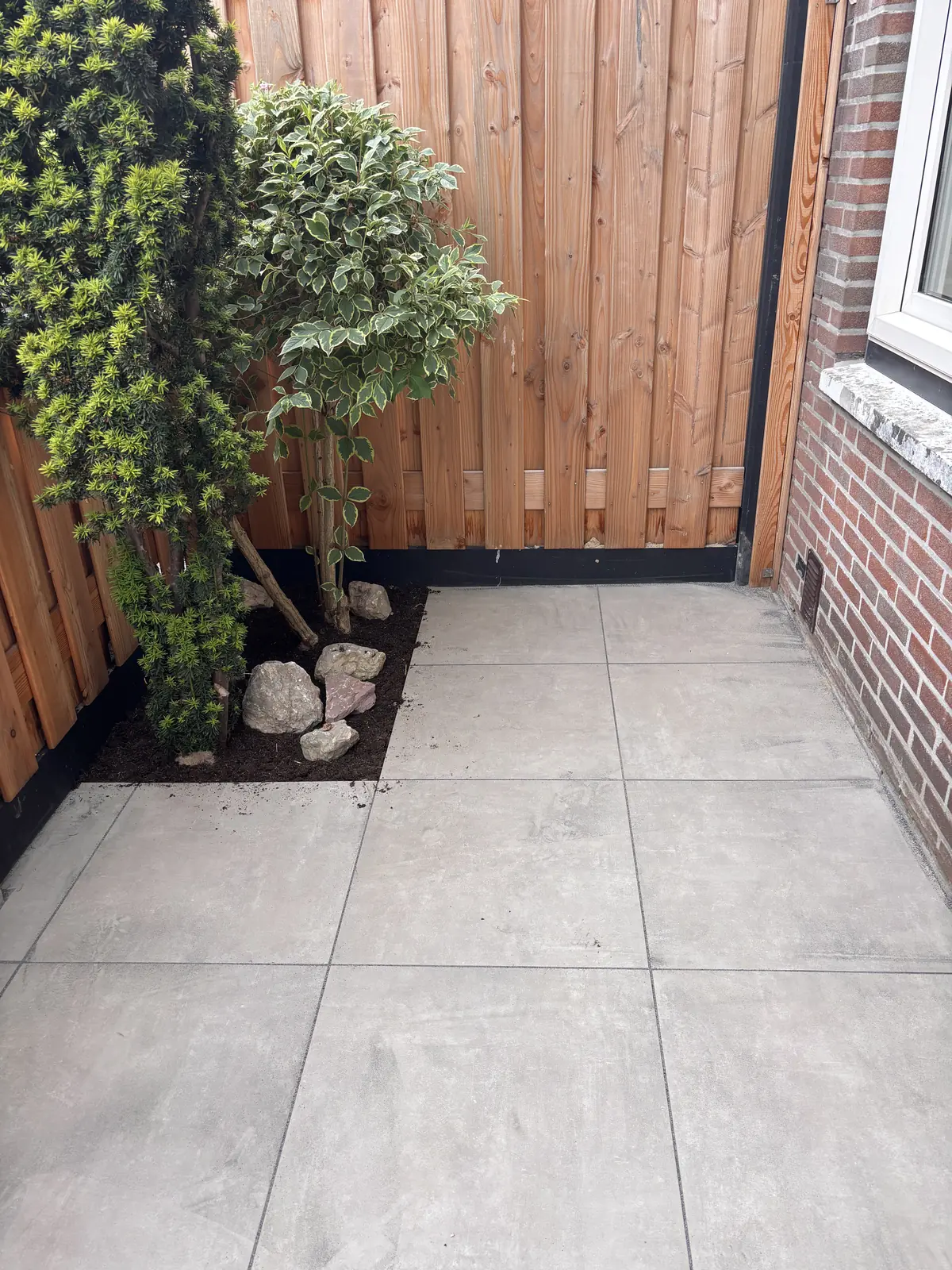 Hoek van het terras met grote lichte tegels tegen de houten schutting