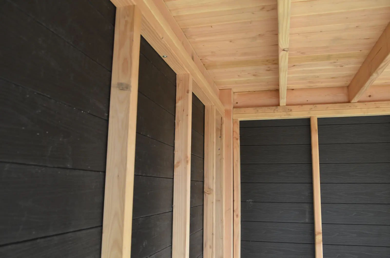 Binnenkant van het tuinhuis: houten staanders en plafond tegen zwarte planken