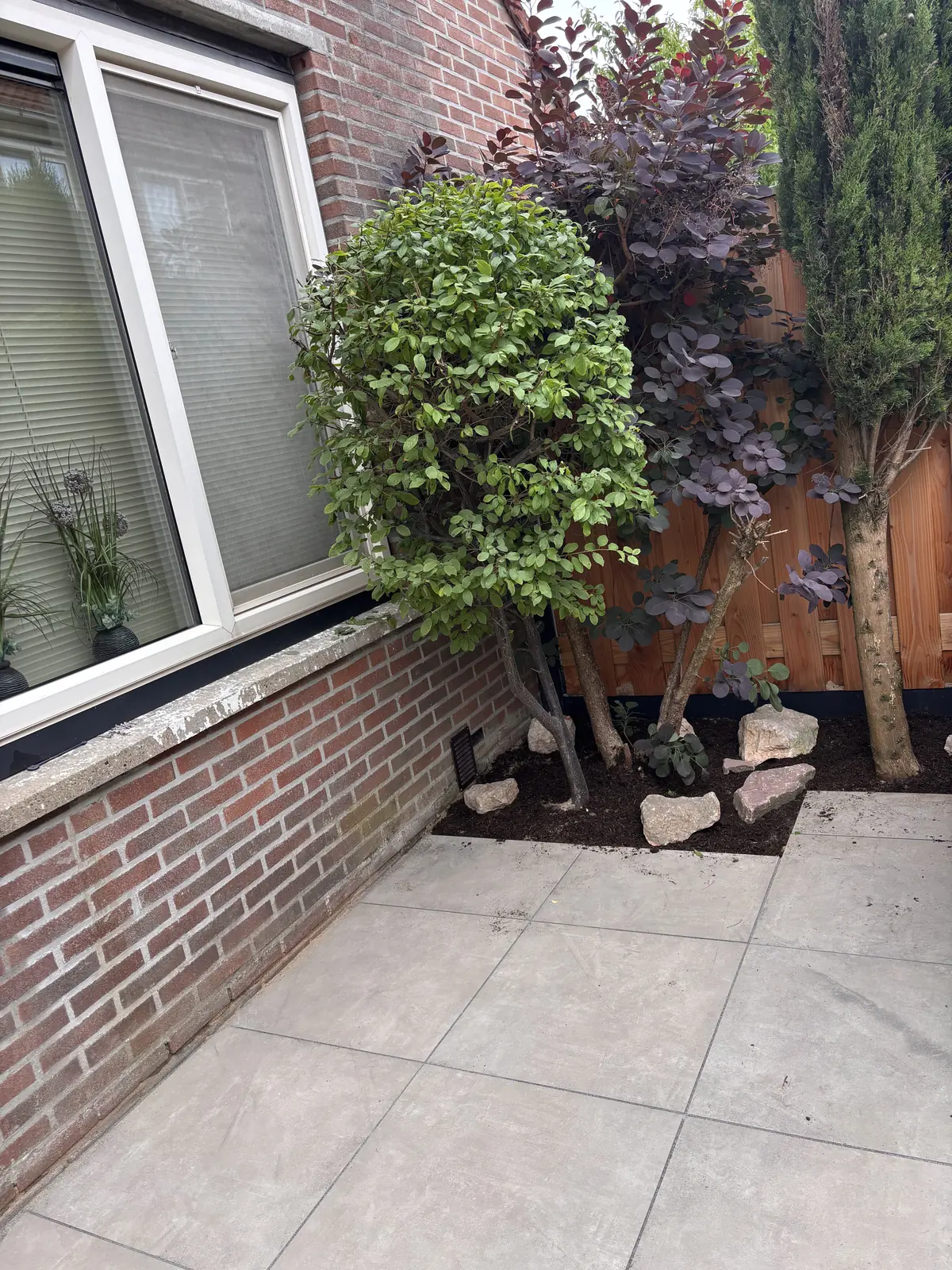 Plantvak met heesters en natuursteen onder het raam, naast het terras