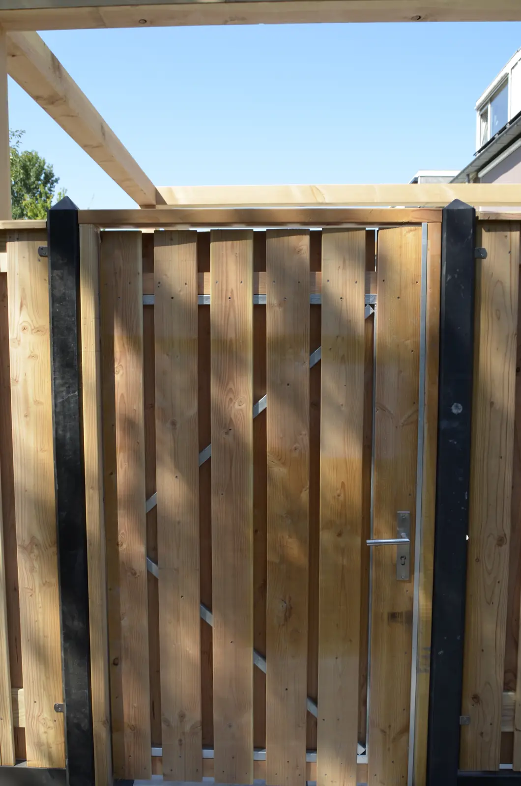 Houten poort tussen antraciet betonpalen, onder de pergola