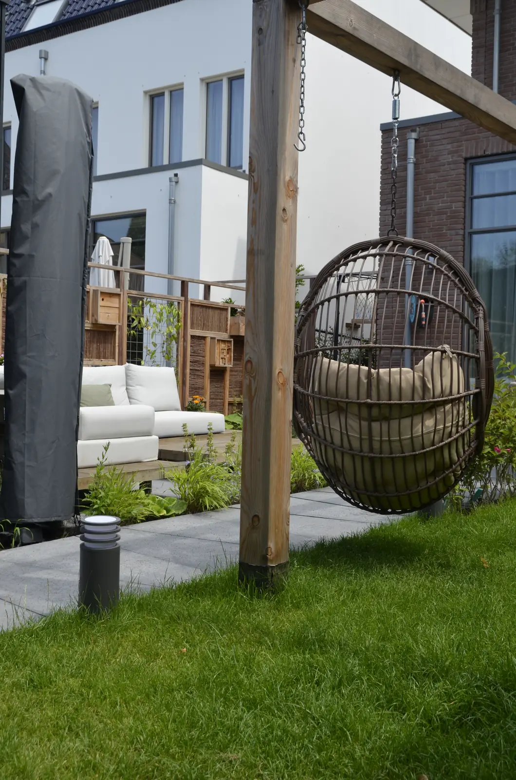 Pergola met hangstoel aan het gazon, de loungeset op het terras erachter