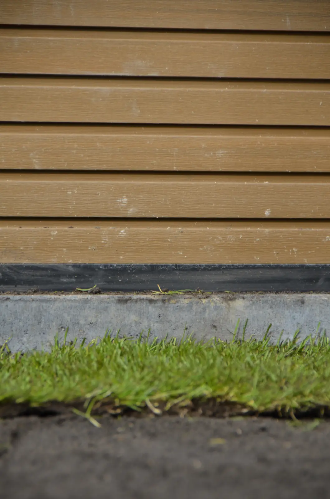 Graszoden tegen de onderrand van de composiet schutting