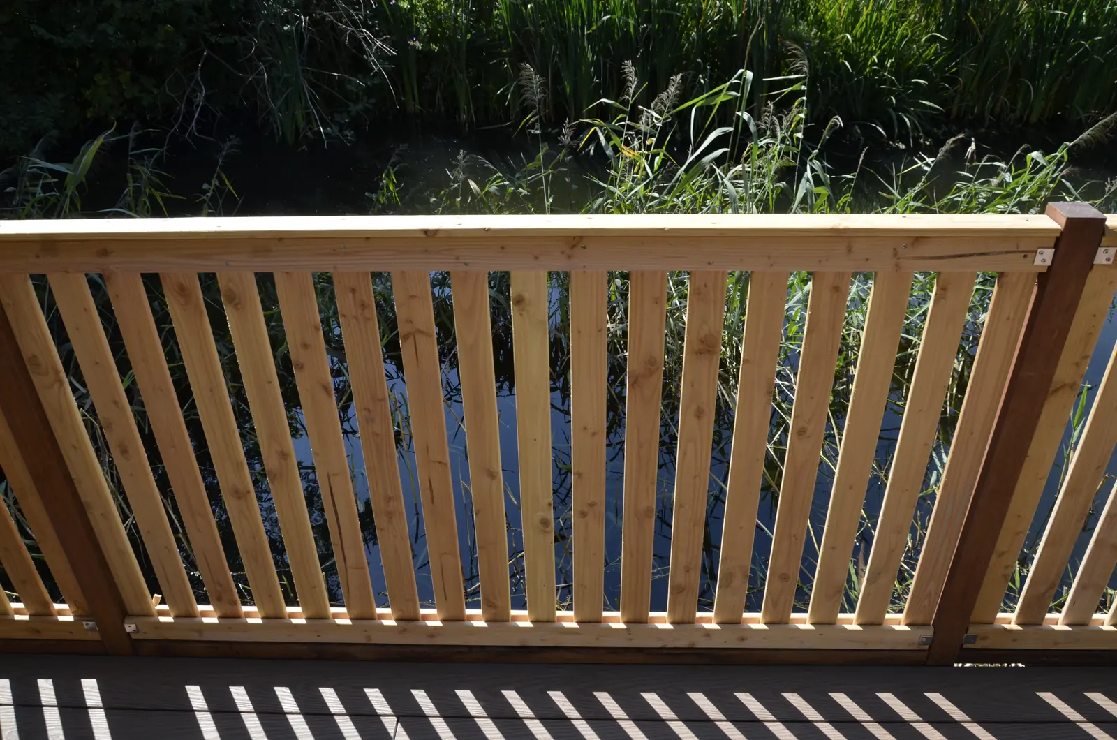 Hekwerk met verticale spijlen tussen de vlonder en het water