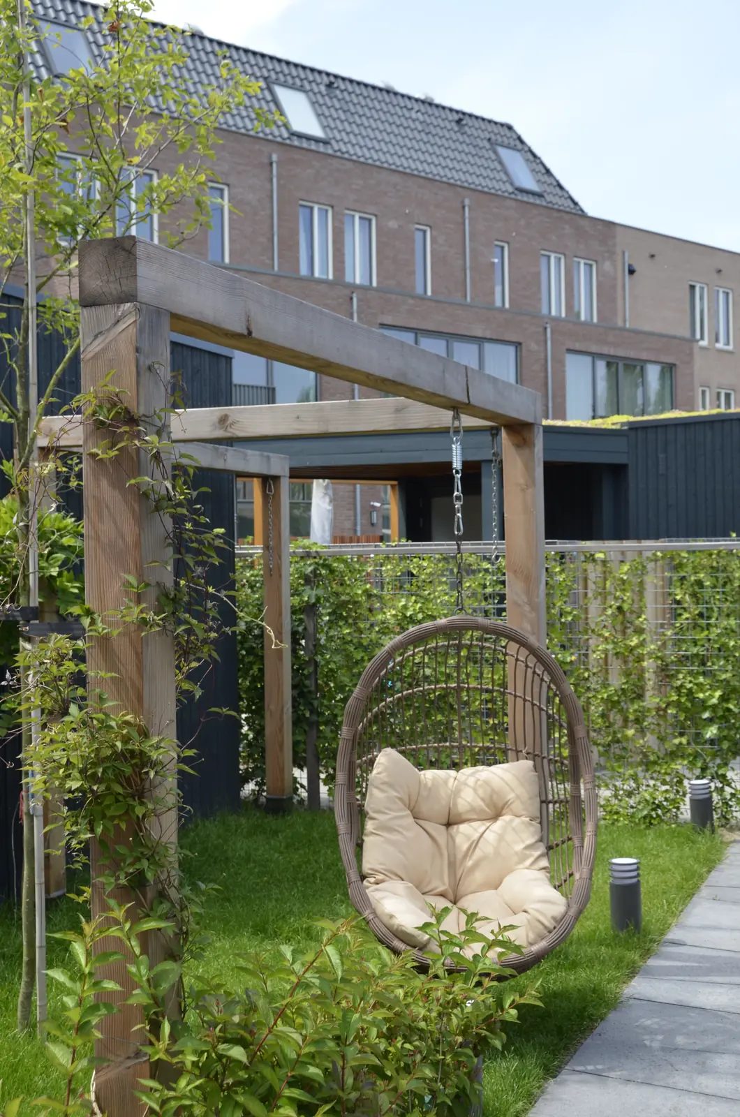 Hangstoel onder de houten pergola, met staande tuinlampen in het gazon