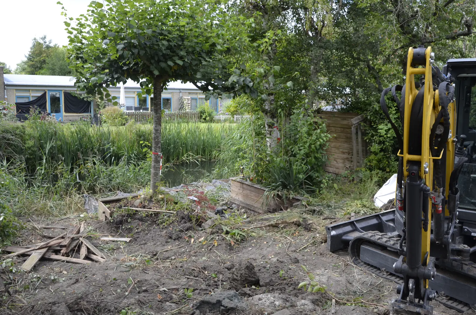 Minigraver in de opgeruimde tuin, met het water en de boom erachter