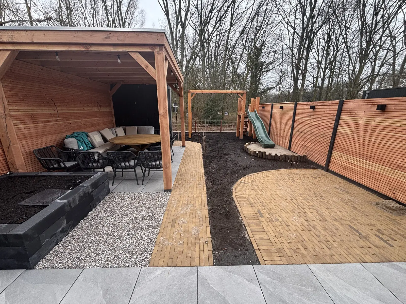 De overkapping met loungeset, het klinkerpad en het gazon